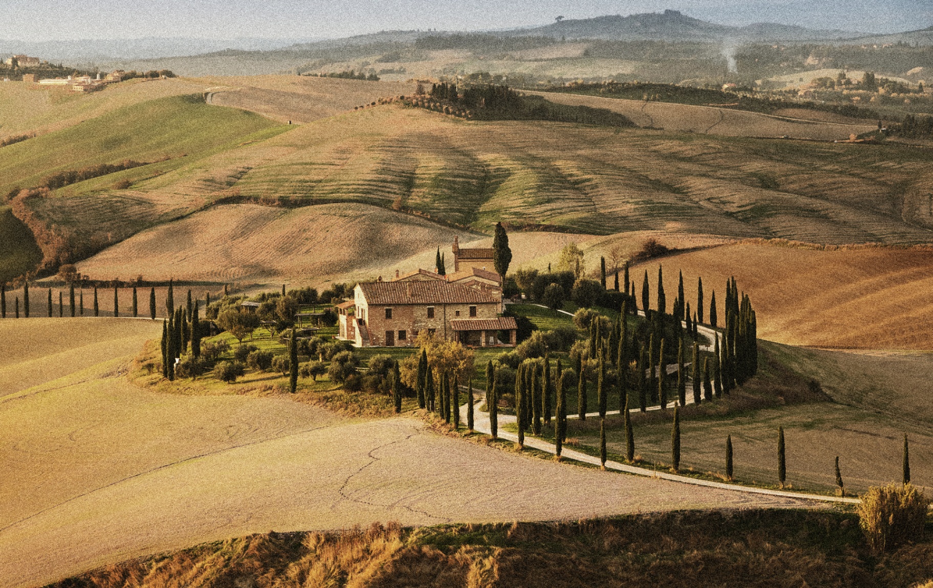 Rolling Tuscan hills with cypress trees and a stone farmhouse